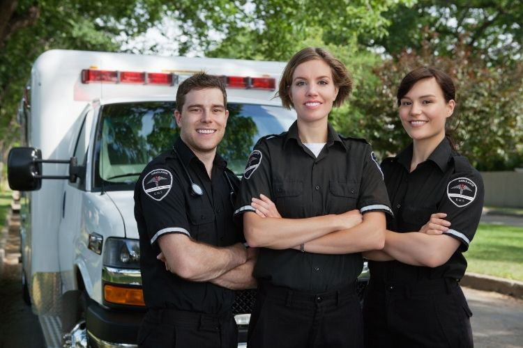 three first responders standing in uniform in front of an ambulance
